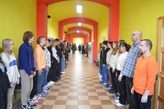 Ludzie stoją w dwóch rzędach naprzeciwko siebie wzdłuż szkolnego korytarza.